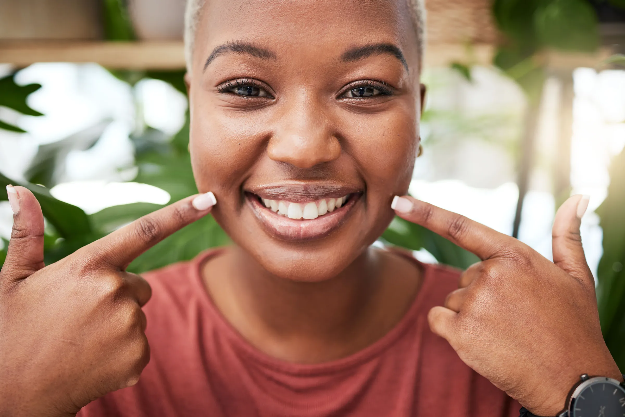 A smiling woman pointing to her front teeth with both index fingers