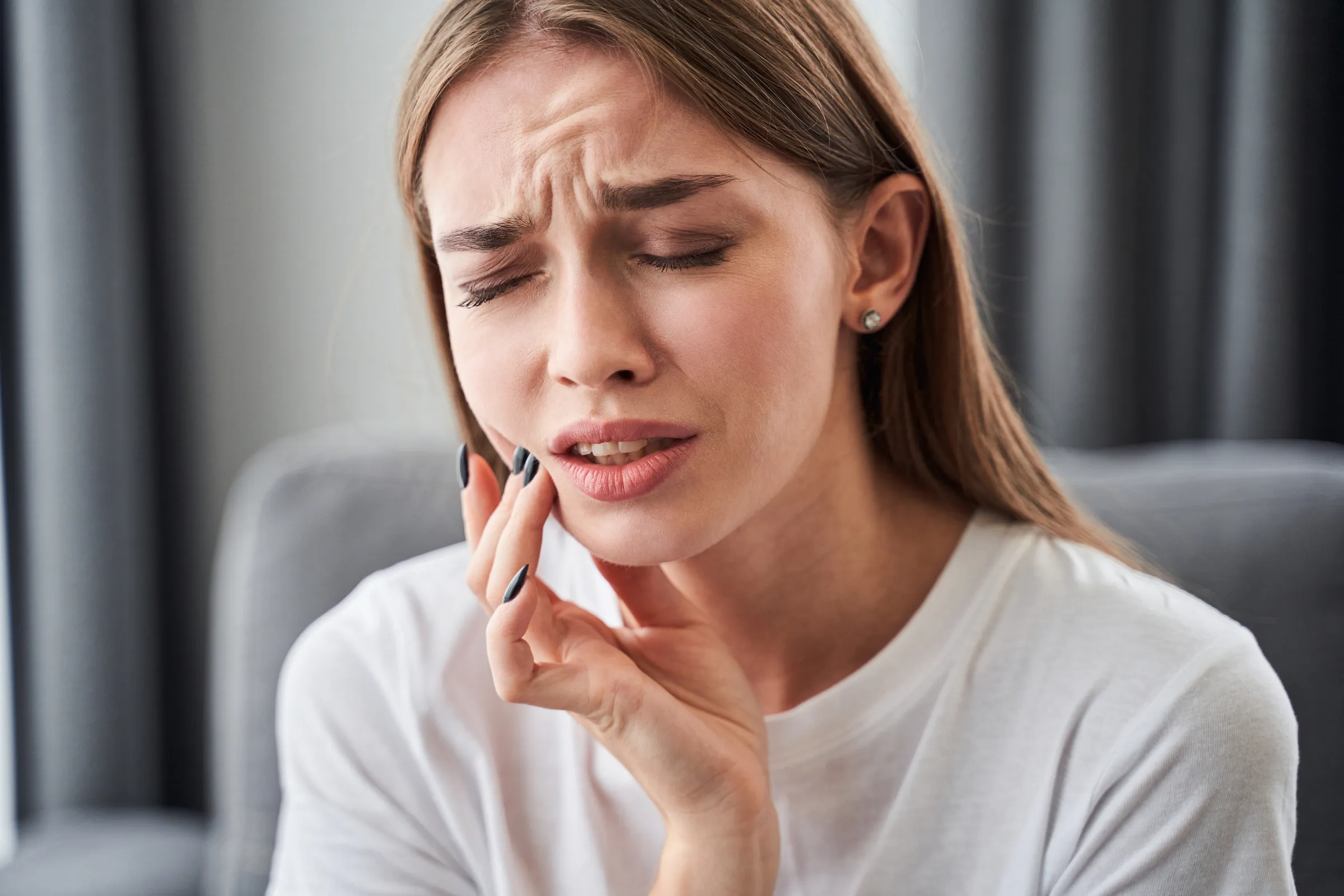 A woman wincing and holding her cheek from tooth pain