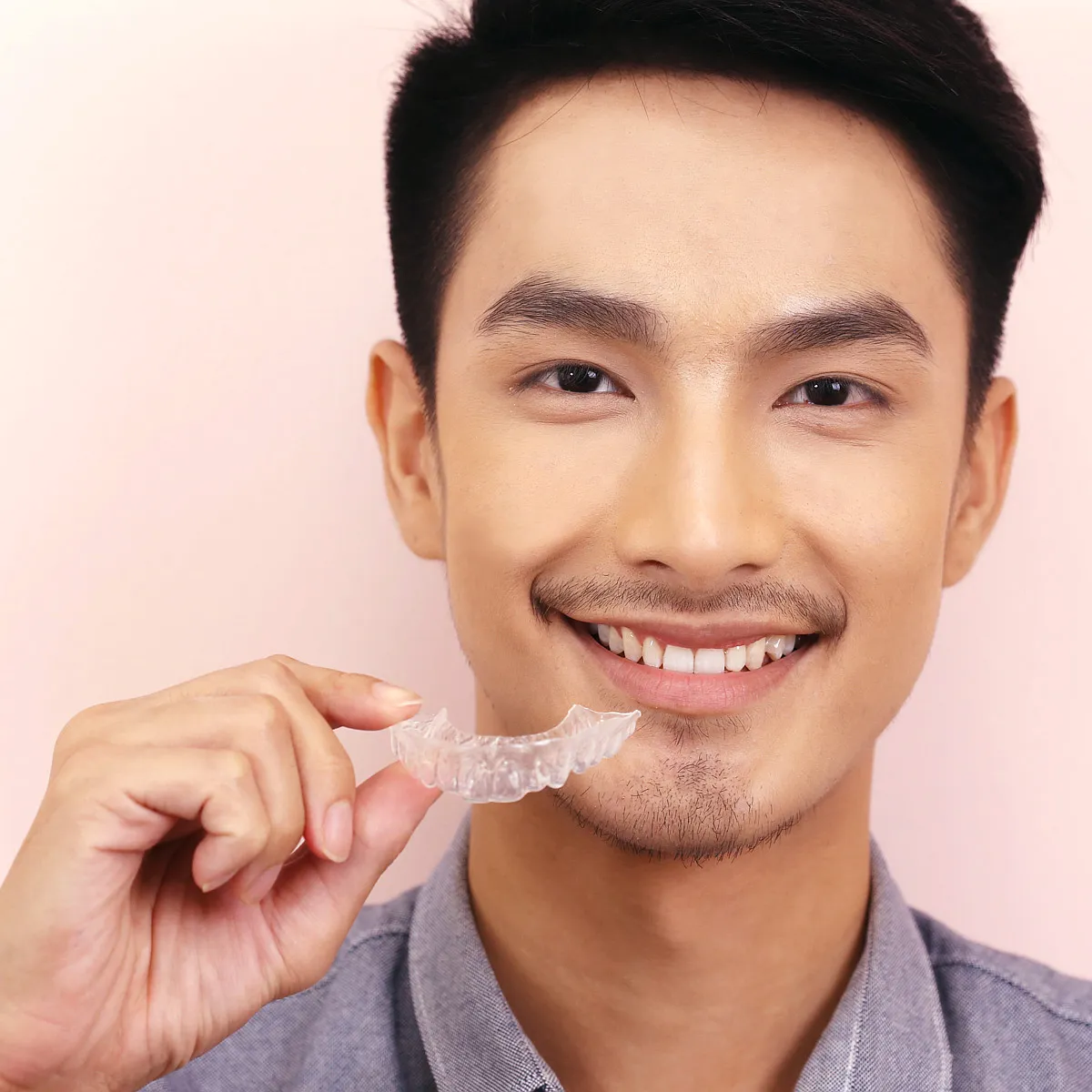A man holding a clear aligner tray beside his smile