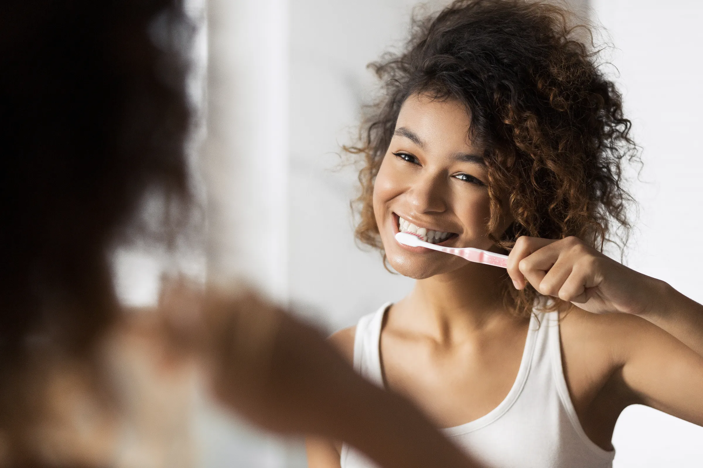 A woman brushing her teeth at a bathroom mirror