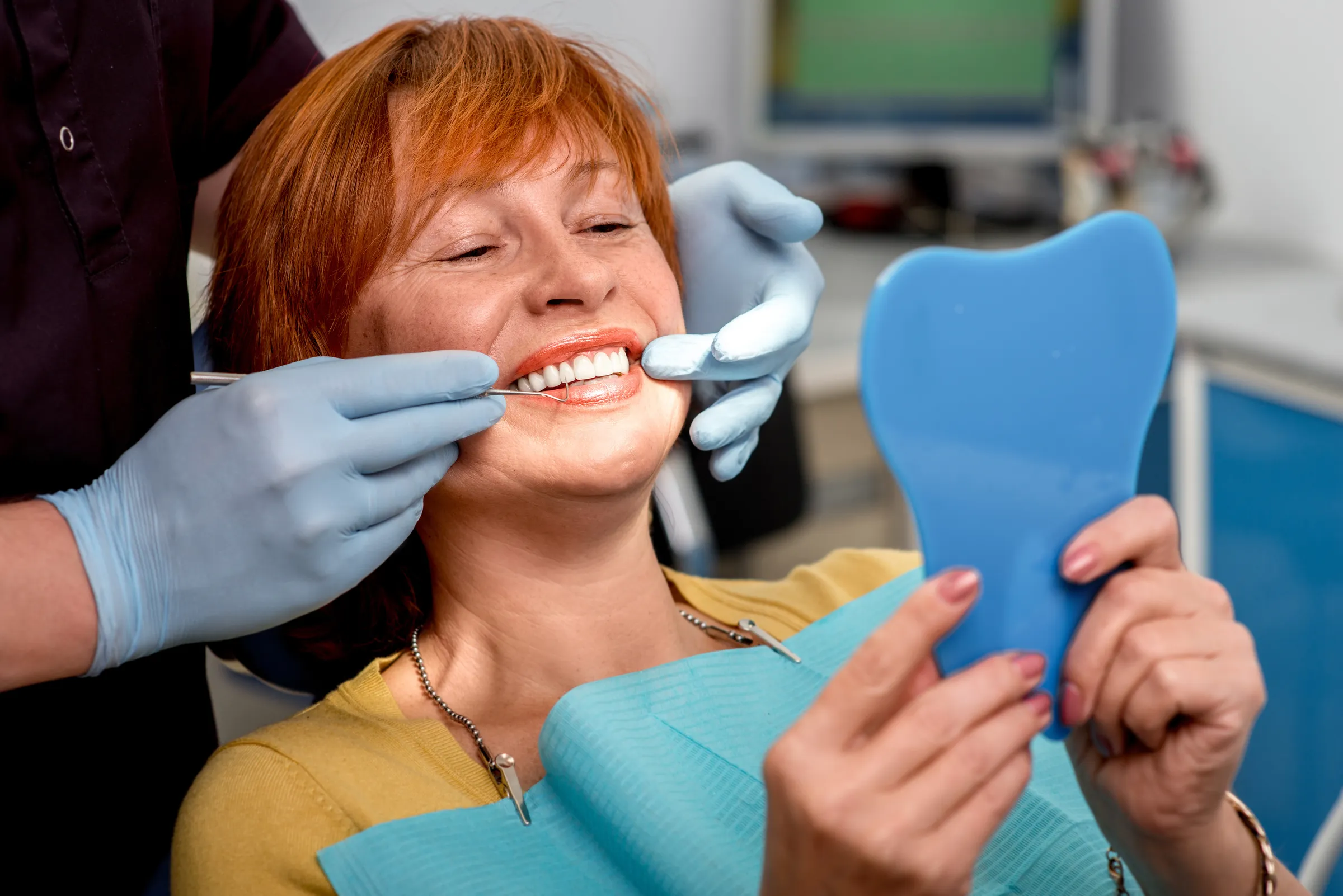 A patient holding a hand mirror while her dentist checks the fit of a denture