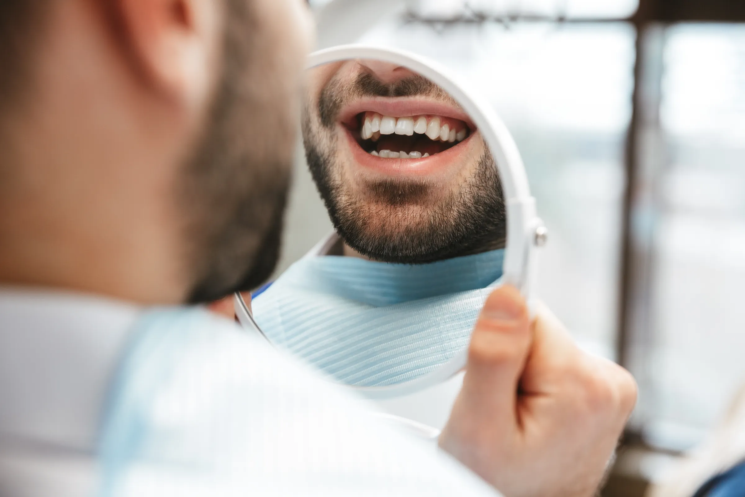 A patient checking his teeth in a hand mirror after treatment