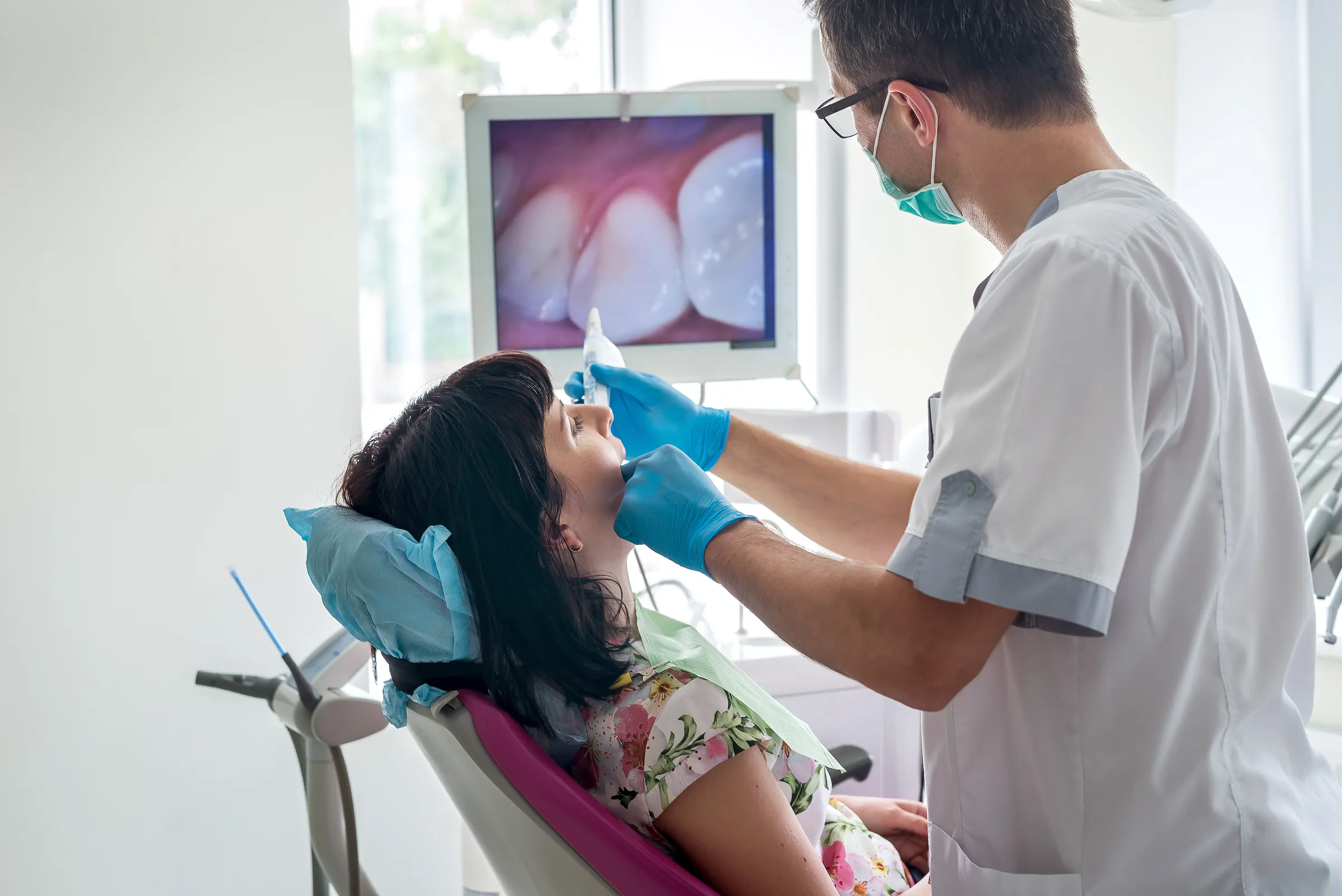 A dentist using an intraoral camera, with the live image shown on a monitor