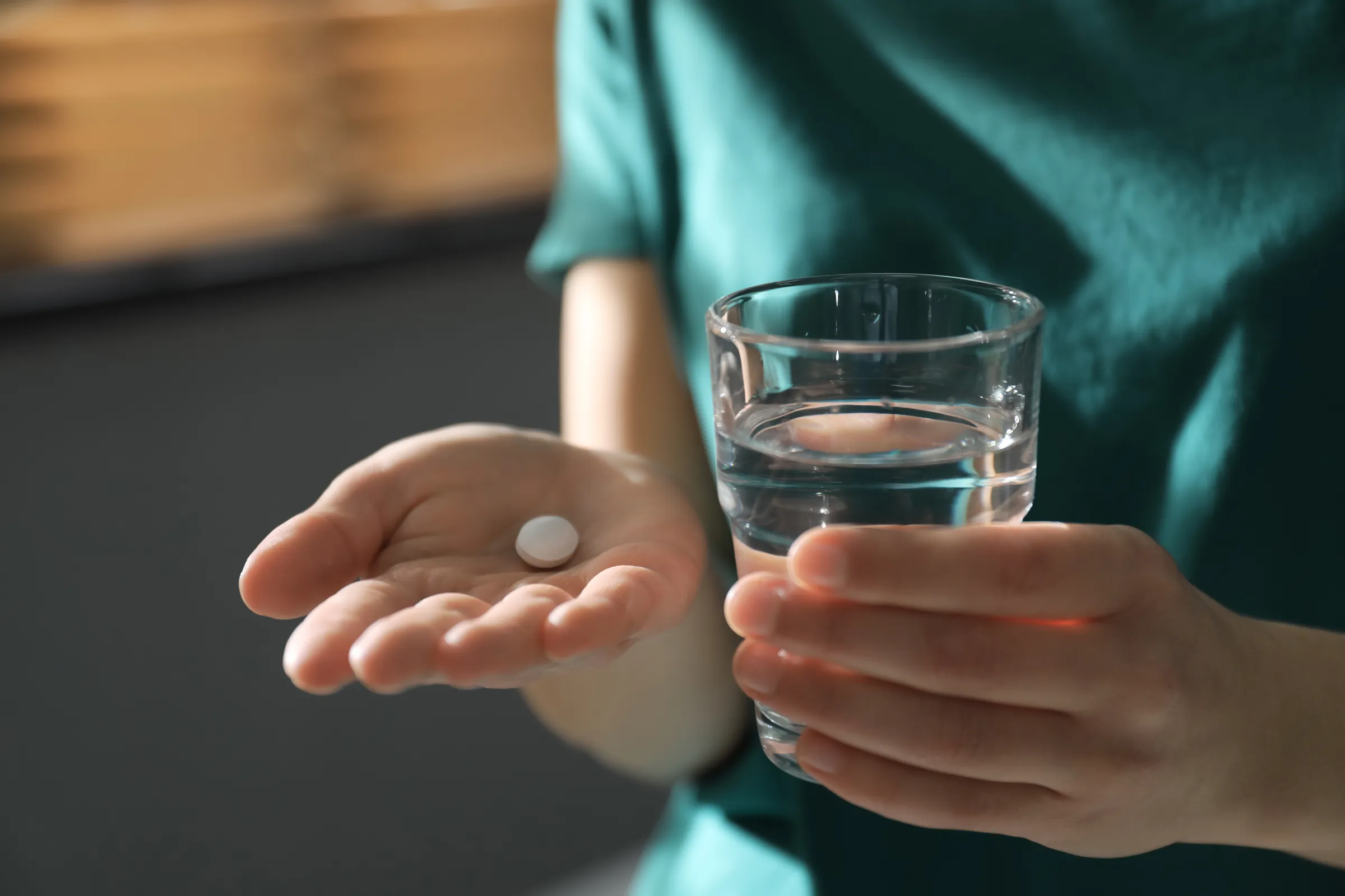 A hand holding a single tablet and a glass of water