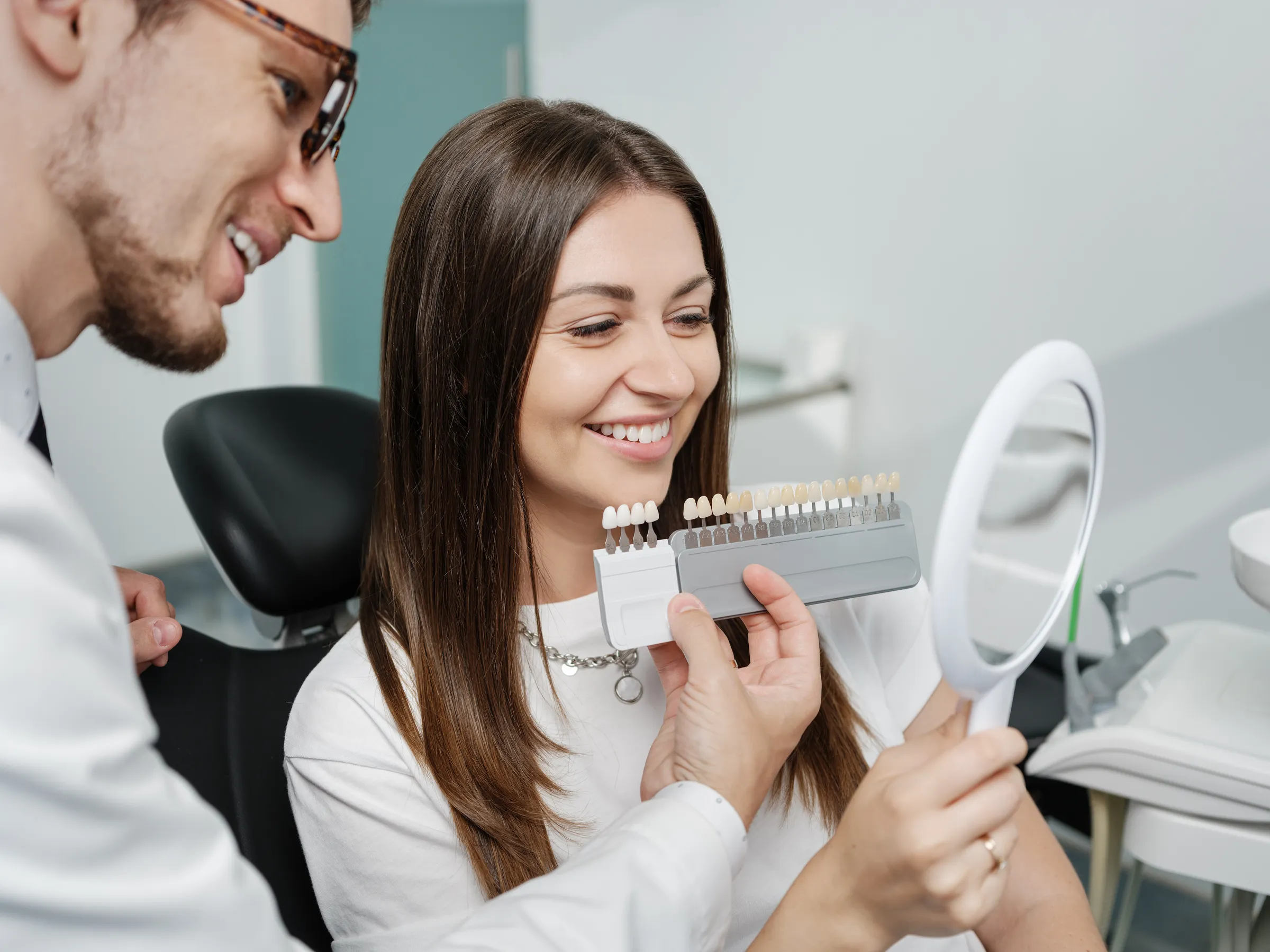 A dentist and patient comparing tooth shades with a shade guide and mirror